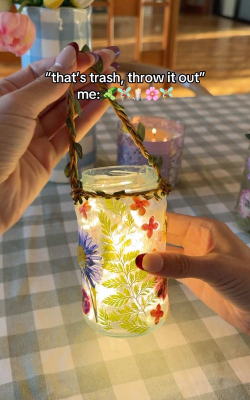 Pickle jar fairy lanterns 🧚‍♀️ I may just have to save all my old jars after trying this craft, I’m in love!! ✨  Clean and dry your jars, then brush on mod podge. Stick the pressed flowers to the outside of the jar, then coat again in mod podge. Allow to dry fully before using. I tied a piece of floral string to the neck of the jar for the handle, then added some twinkle lights inside.  #diy #cozyhome #cottagecore #upcycle #cozyhobbies 