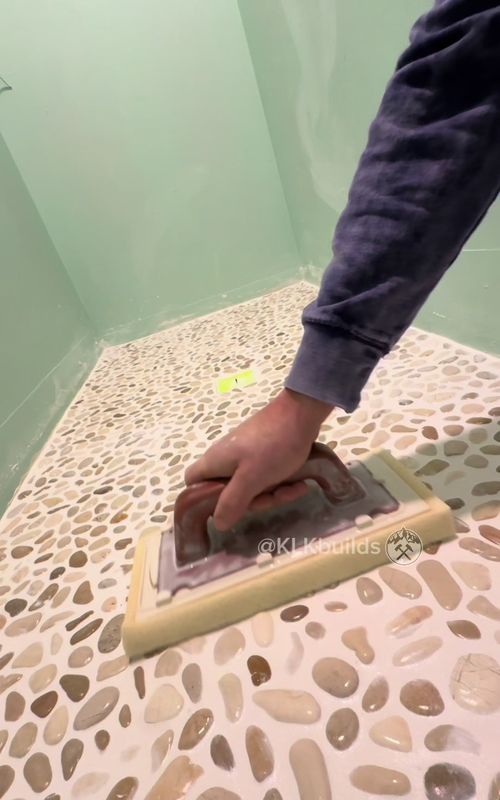 Grouting the shower floor pebble tiles.  I like to tile and grout my shower floor first, cover it then tile the walls.  #homeimprovement #tile #grout #construction #diy 