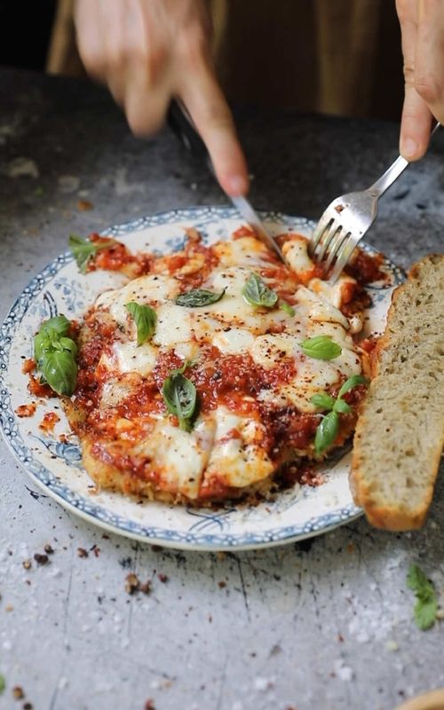 Potato-Crusted Chicken Parmigiana 😋 recipe below! #food    Potato-Crusted Chicken Parmesan   Ingredients: For the Tomato Sauce: 2 tbsp olive oil 1 medium yellow onion, diced 2 cloves garlic, minced 28 oz San Marzano crushed tomatoes 1 ¼ tsp salt, more to taste 1 tsp dried or 1 tbsp fresh oregano 1 tbsp fresh basil 1 tsp sugar ¼ tsp garlic salt ½ cup water or chicken broth   For the Chicken: 3 large or 4 small chicken breasts 2-3 russet potatoes Shredded Parmesan cheese 1 tsp salt 1 tsp ground pepper 2 eggs ½ cup flour ½ tsp salt ½ tsp pepper ½ tsp garlic salt 1 tsp paprika   For Assembly: Olive oil or neutral oil for frying Fresh or shredded mozzarella Freshly shredded Parmesan cheese Fresh basil   Instructions: Heat a medium saucepan over medium heat. Add olive oil and onion and sauté for 4-5 minutes until softened. Add minced garlic and cook for 1 more minute. Add tomatoes, salt, oregano, basil, sugar, and garlic salt. Continue to cook for 2-3 minutes, stirring occasionally, until everything comes together. Add water or chicken broth, stir together and turn to medium low heat. Cook for 15-20 minutes until onions are full cooked and the sauce becomes your preferred texture, adding additional chicken broth or water as necessary. Remove from heat and set aside.   Using a sharp knife, slice the chicken into thin filets. You can also cut the filets in half if you prefer. Place the chicken on a work surface and cover with parchment paper. Pound the chicken with a meat tenderizer until it’s about ¼” thick. Remove the parchment paper and sprinkle each side with salt and pepper. Let rest for 10-15 minutes.   While the chicken is resting, wash and peel potatoes. Grate the potatoes into fine shreds, then transfer the shredded potatoes into a bowl of ice water. Rinse the potatoes in the water to flush out most of the starch. Transfer the potatoes into a cheesecloth (paper towels also work), wrapping them tightly and gently squeezing to remove any excess water.   In three shallow bowls, place shredded potato, eggs, and flour. Add shredded parmesan into the potatoes and mix. Mix ½ tsp garlic salt into the flour and beat ½ tsp salt and pepper into the eggs. Place the first chicken cutlet into the flour mixture and coat well. Then dredge with the egg mixture and coat well. Finally, coat the cutlet fully with the shredded potatoes, pressing them firmly to ensure they adhere. Place the coated chicken breast onto a wire rack and repeat until each piece of chicken is fully coated.   Heat ½ inch of oil in a large pan over medium high heat. Carefully place a piece of chicken into the hot oil and fry for 3-4 minutes on each side until golden browned and crispy. Remove onto a clean cooling rack and repeat with each piece of chicken, maintaining the oil level with additional oil and letting heat before cooking the next pieces.   Meanwhile, set the oven to broil. Spoon sauce into an oven-safe dish or tray. Top with mozzarella and parmesan cheeses, then sprinkle on fresh basil leaves. Broil the sauce just until the cheese has melted. Remove from the oven and pour the sauce and cheese carefully over the chicken as shown in the reel. Top with additional basil, olive oil, and chili flakes, if desired. Serve with fresh focaccia.   Bon appetit!
